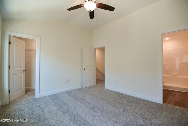 unfurnished bedroom with connected bathroom, a walk in closet, vaulted ceiling, ceiling fan, and light colored carpet