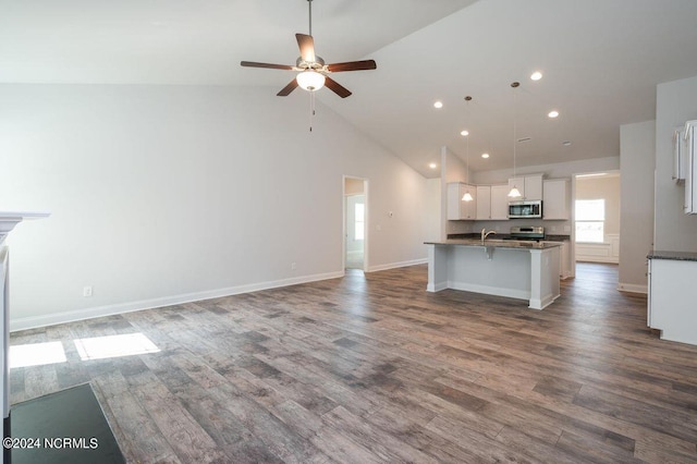 kitchen with appliances with stainless steel finishes, open floor plan, a kitchen island with sink, white cabinets, and a kitchen bar