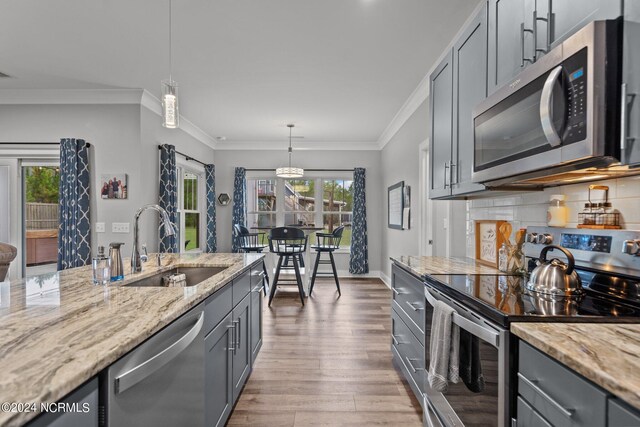 kitchen with crown molding, sink, light stone countertops, light hardwood / wood-style floors, and appliances with stainless steel finishes