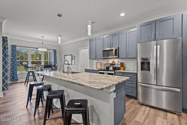 kitchen featuring stainless steel appliances, light stone counters, a kitchen island with sink, and light wood-type flooring