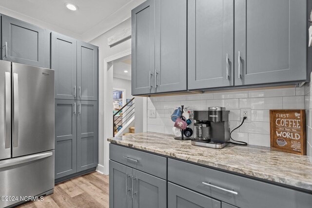 kitchen with stainless steel fridge, tasteful backsplash, light stone counters, and light wood-type flooring