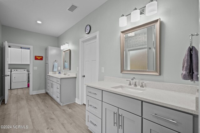 bathroom featuring dual vanity, washing machine and dryer, and hardwood / wood-style flooring