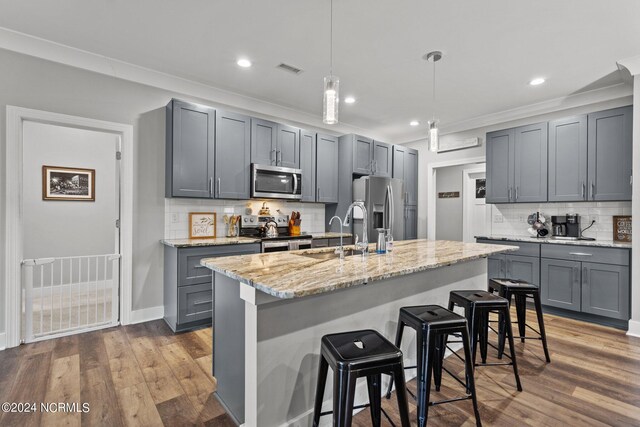 kitchen featuring appliances with stainless steel finishes, gray cabinetry, light stone counters, backsplash, and hardwood / wood-style flooring