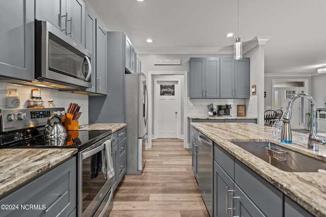 kitchen with stainless steel appliances, sink, light stone countertops, light hardwood / wood-style flooring, and backsplash