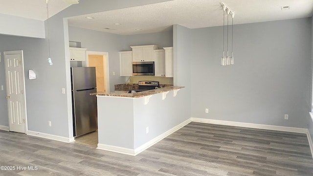 kitchen with pendant lighting, appliances with stainless steel finishes, white cabinetry, light hardwood / wood-style floors, and kitchen peninsula