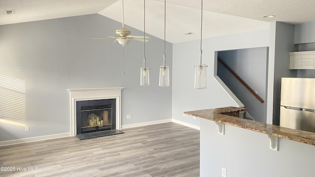 unfurnished living room with lofted ceiling, a textured ceiling, ceiling fan, and light hardwood / wood-style flooring