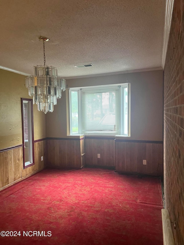 carpeted spare room featuring crown molding, wood walls, a textured ceiling, and a notable chandelier