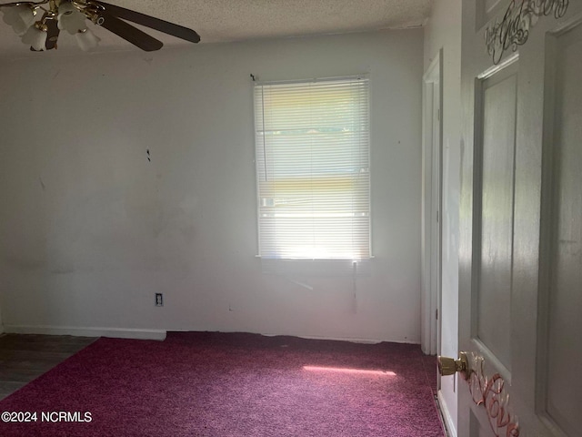 spare room featuring ceiling fan, dark carpet, and a textured ceiling