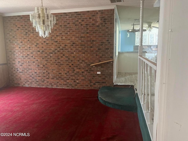 unfurnished dining area with brick wall, carpet, a textured ceiling, ornamental molding, and a notable chandelier