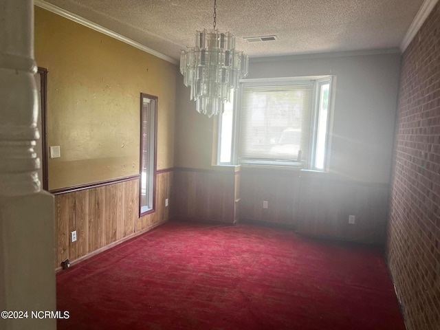 carpeted empty room featuring crown molding, a textured ceiling, wooden walls, and a notable chandelier