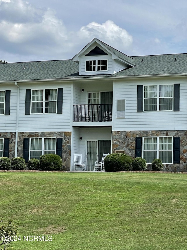 view of front of house with stone siding, a front yard, and a balcony