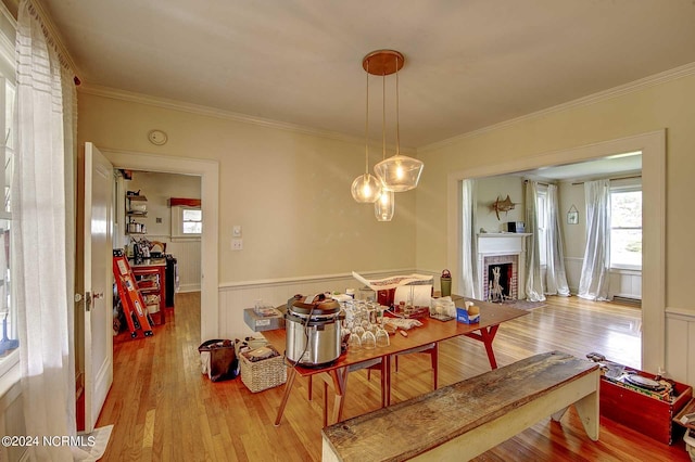 dining area featuring crown molding, a brick fireplace, and light hardwood / wood-style flooring