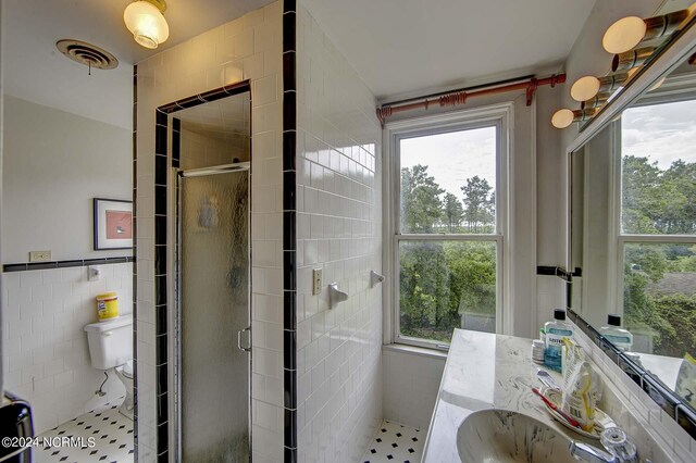 bathroom with a shower with door, vanity, tile walls, and toilet