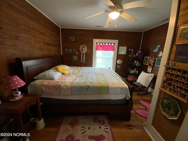 bedroom with hardwood / wood-style flooring, ceiling fan, and wood walls