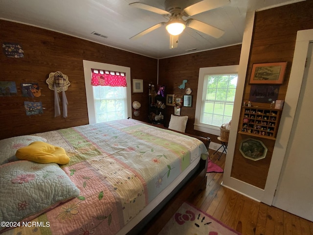 bedroom with hardwood / wood-style flooring, wooden walls, and ceiling fan