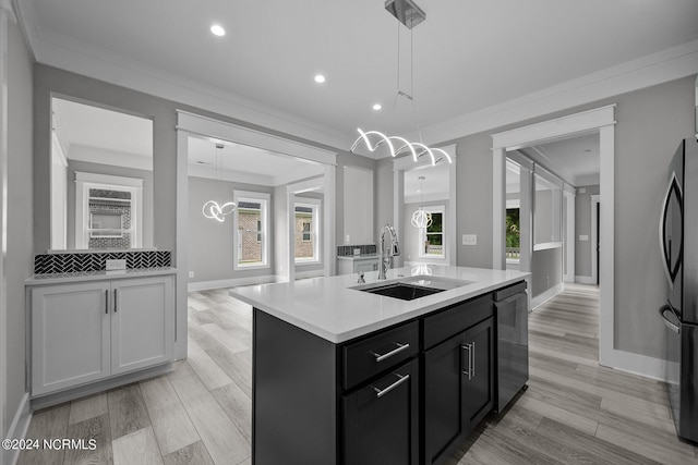 kitchen with appliances with stainless steel finishes, decorative light fixtures, sink, a kitchen island with sink, and light hardwood / wood-style floors