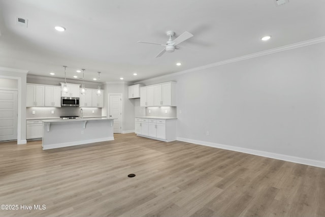 kitchen with ceiling fan, backsplash, light hardwood / wood-style floors, white cabinets, and a center island with sink