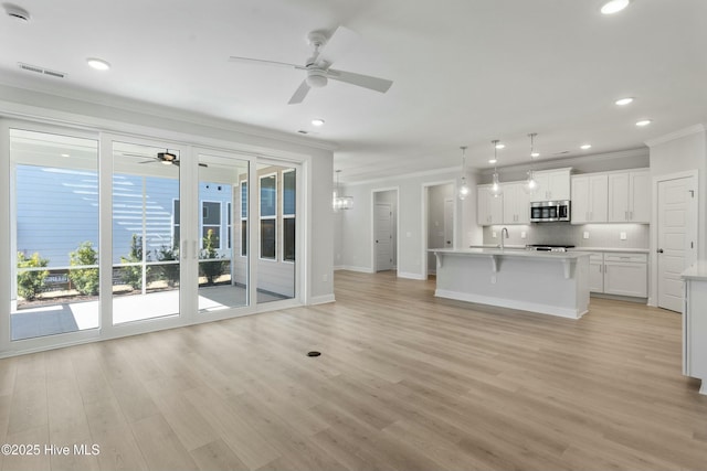 unfurnished living room with sink, ornamental molding, ceiling fan, and light wood-type flooring