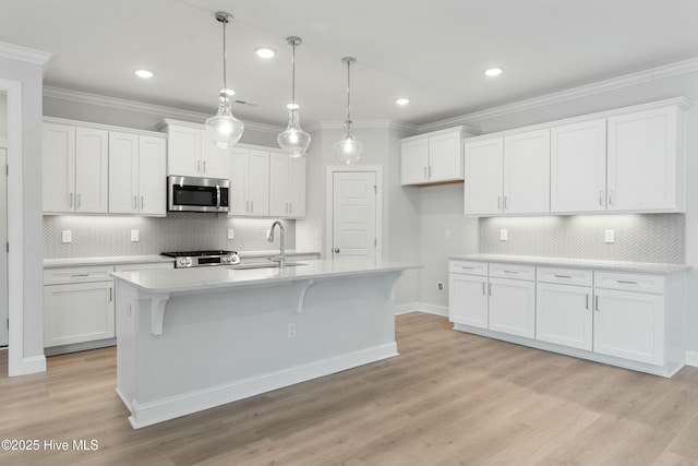 kitchen with white cabinetry, decorative light fixtures, a center island with sink, and crown molding