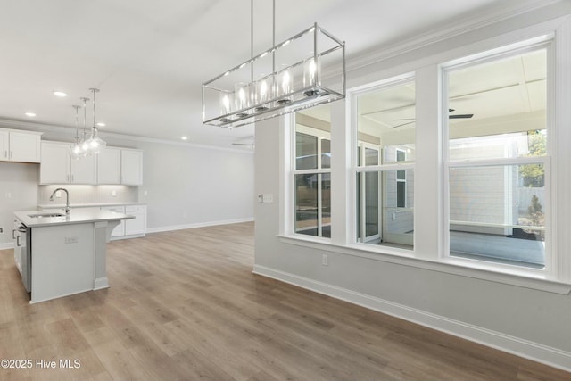 kitchen with pendant lighting, sink, white cabinetry, ornamental molding, and an island with sink