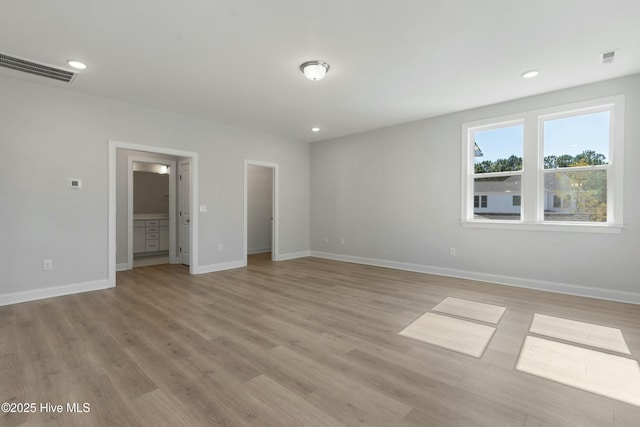 unfurnished bedroom featuring connected bathroom, a spacious closet, and light wood-type flooring