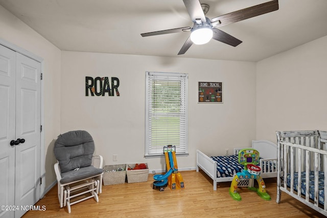 bedroom featuring a crib, hardwood / wood-style flooring, ceiling fan, and a closet