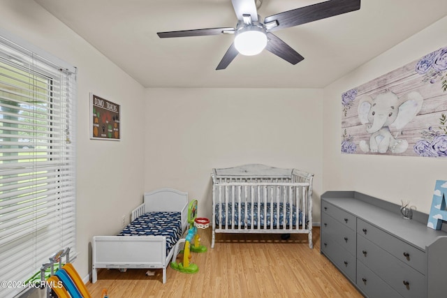 bedroom featuring a crib, ceiling fan, and light hardwood / wood-style flooring