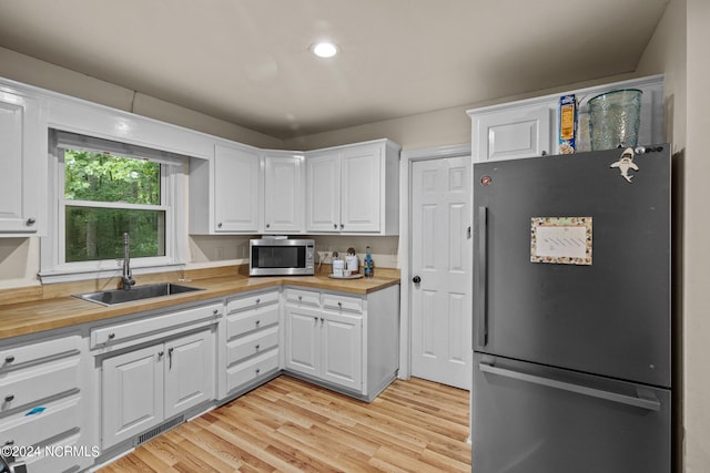 kitchen with stainless steel appliances, white cabinetry, sink, and wooden counters