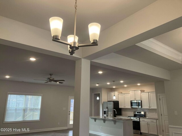 kitchen featuring stainless steel appliances, an island with sink, light stone countertops, decorative light fixtures, and tasteful backsplash