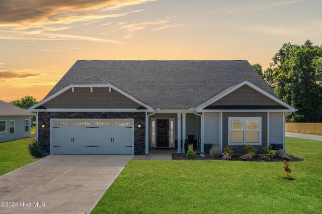 craftsman-style home with a garage, stone siding, concrete driveway, and a yard