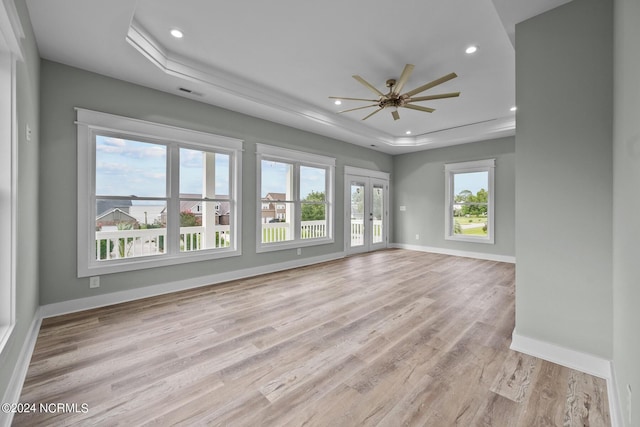 empty room with a tray ceiling, light hardwood / wood-style floors, french doors, and ceiling fan