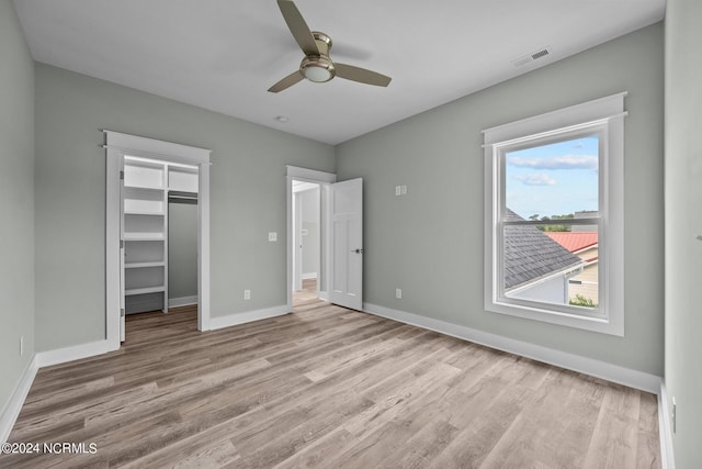 unfurnished bedroom with a spacious closet, light hardwood / wood-style flooring, a closet, and ceiling fan