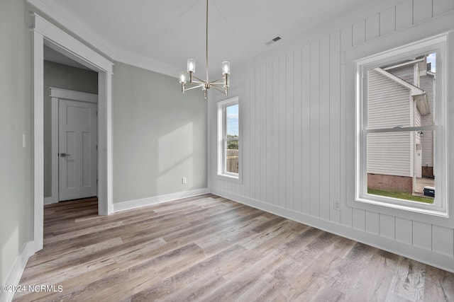 unfurnished room with an inviting chandelier, crown molding, and light wood-type flooring