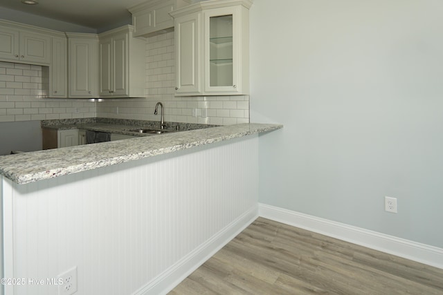 kitchen featuring light stone countertops, sink, kitchen peninsula, and decorative backsplash