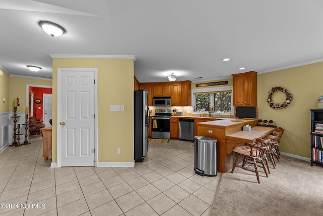 kitchen featuring appliances with stainless steel finishes, light tile patterned flooring, brown cabinets, and crown molding