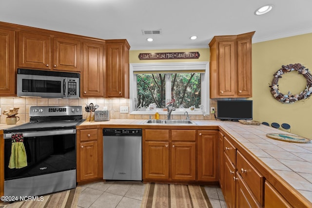 kitchen with tasteful backsplash, appliances with stainless steel finishes, tile counters, and sink