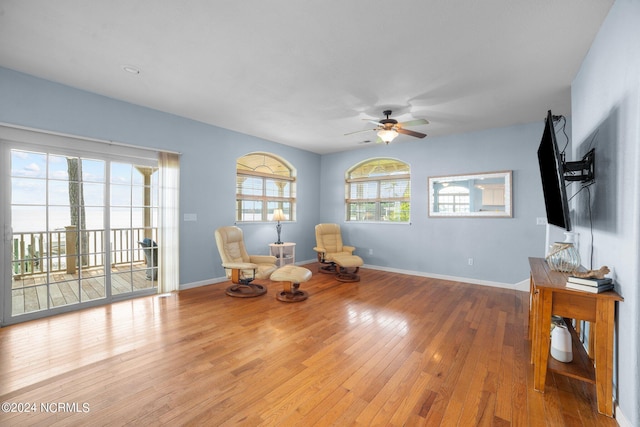 living area featuring wood-type flooring, a ceiling fan, and baseboards