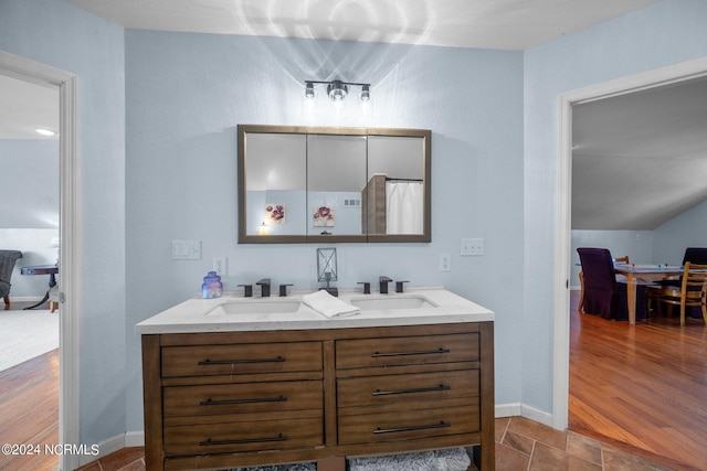 full bath featuring double vanity, wood finished floors, a sink, and baseboards