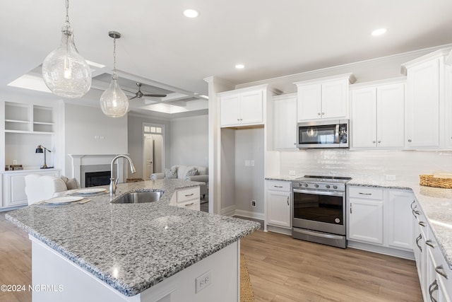 kitchen with appliances with stainless steel finishes, light wood-type flooring, a fireplace, white cabinetry, and a sink