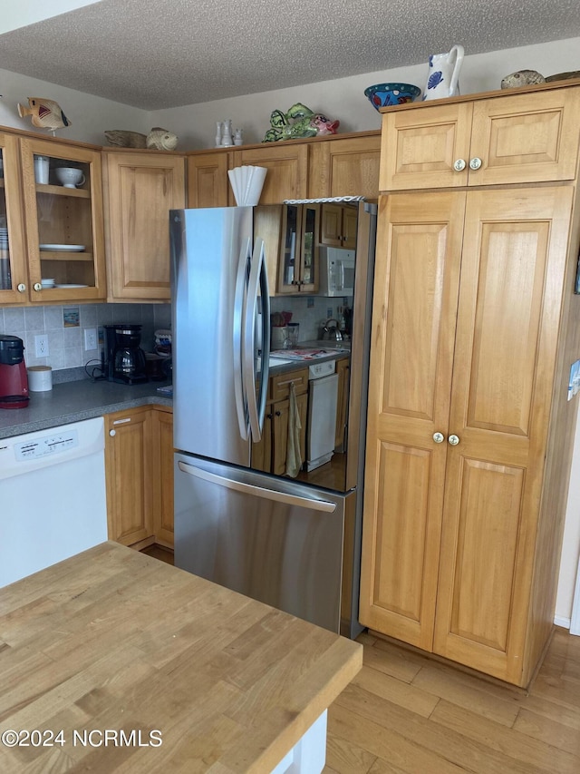 kitchen with backsplash, a textured ceiling, light hardwood / wood-style floors, and white appliances