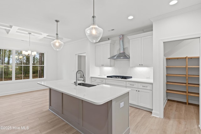 kitchen featuring a kitchen island with sink, stainless steel gas cooktop, white cabinetry, light countertops, and wall chimney exhaust hood