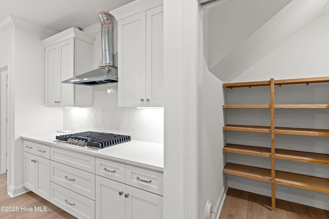 kitchen featuring stainless steel gas cooktop, light wood-style floors, white cabinets, light countertops, and wall chimney range hood