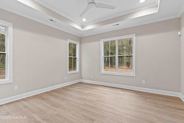 unfurnished room with a tray ceiling, crown molding, light wood-style flooring, and baseboards