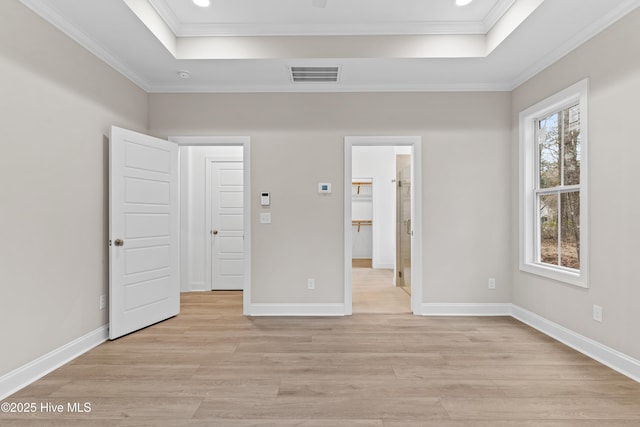 unfurnished bedroom with crown molding, a tray ceiling, visible vents, and light wood-style floors