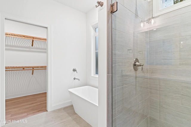 bathroom with a freestanding tub, a shower stall, a walk in closet, and baseboards