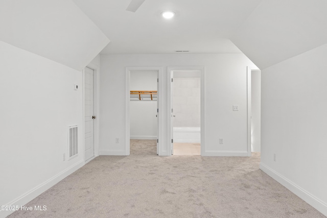 additional living space featuring light carpet, visible vents, and baseboards