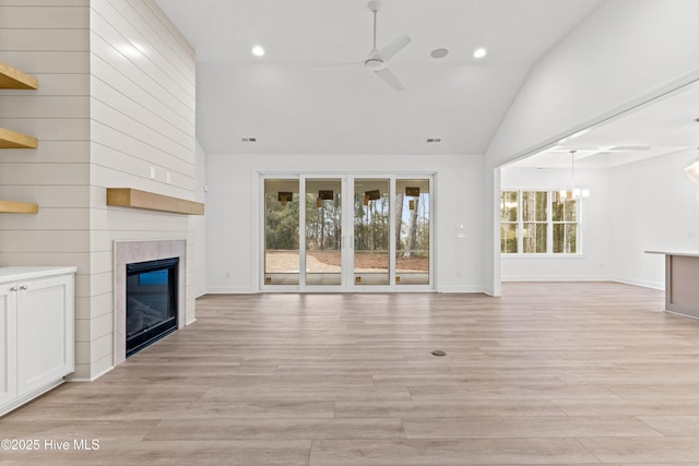 unfurnished living room featuring ceiling fan with notable chandelier, high vaulted ceiling, a tile fireplace, and light wood-style floors