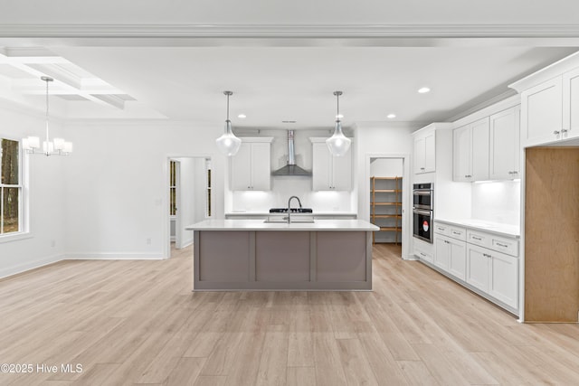 kitchen featuring wall chimney exhaust hood, white cabinetry, light countertops, and decorative light fixtures