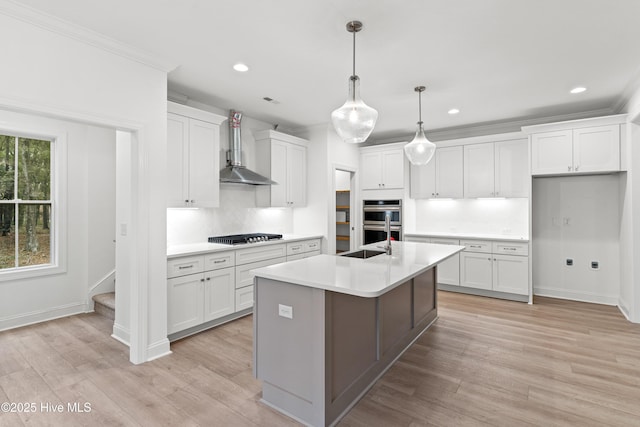 kitchen with light countertops, wall chimney range hood, an island with sink, and white cabinets