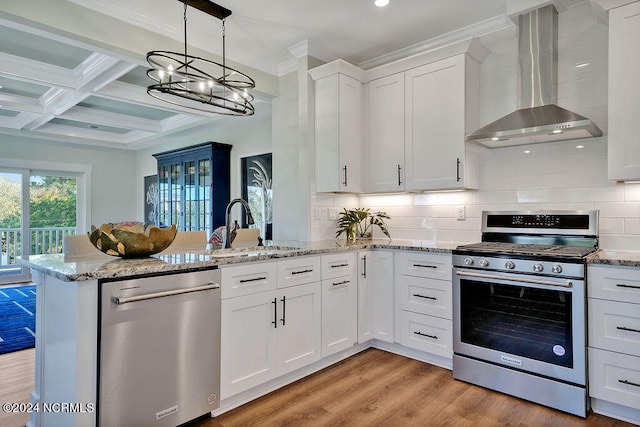 kitchen with coffered ceiling, white cabinetry, appliances with stainless steel finishes, kitchen peninsula, and wall chimney range hood